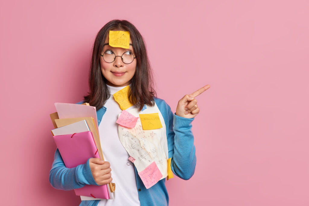 horizontal shot of brunette asian woman manager examines paper documents points away on blank space works on startup project isolated over pink background. check this out. education and studying horizontal shot of brunette asian woman manager examines paper documents points away on blank space works on startup project isolated over pink background. check this out. education and studying