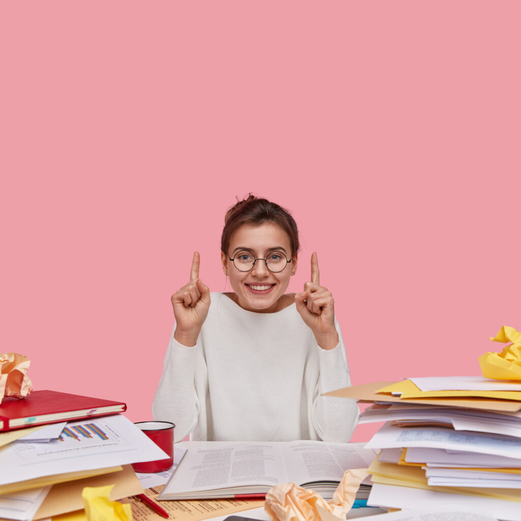 positive european woman with glad facial expression, dressed in white casual clothes, shows direction upside, uses paper documents, has toothy smile, isolated over pink background, reads books positive european woman with glad facial expression, dressed in white casual clothes, shows direction upside, uses paper documents, has toothy smile, isolated over pink background, reads books